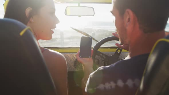 Happy caucasian couple sitting in beach buggy by the sea using smartphone