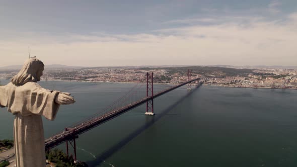 Panoramic orbiting shot around the statue of Christ the King overlooking Lisbon cityscape.