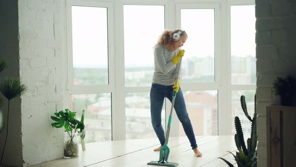 Beautiful Young Woman Is Cleaning Light Modern Studio with Panoramic Windows, Girl Is Washing Floor