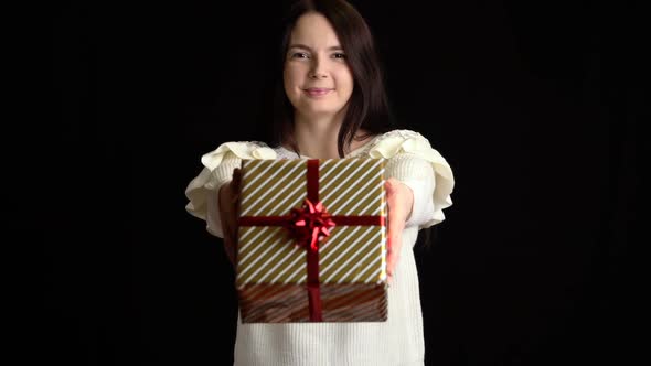 Young Woman Gives a Gift Box on Black Background. Gift Box with White Ribbon for Happy New Year