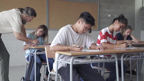 Asian Student Taking Exam and Professor Explaining Exercise to Teenager Pupil in Secondary School