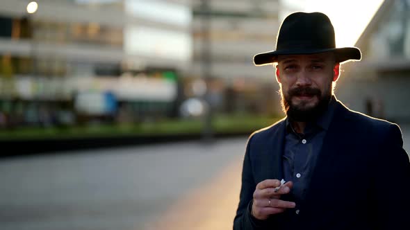 Handsome Man with Hat Moustache and Cigarette is Looking Cunningly to Camera