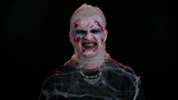 Zombie Man with Wounds Scars and Contact Lenses Looking at Camera Clicks His Teeth Trying to Scare