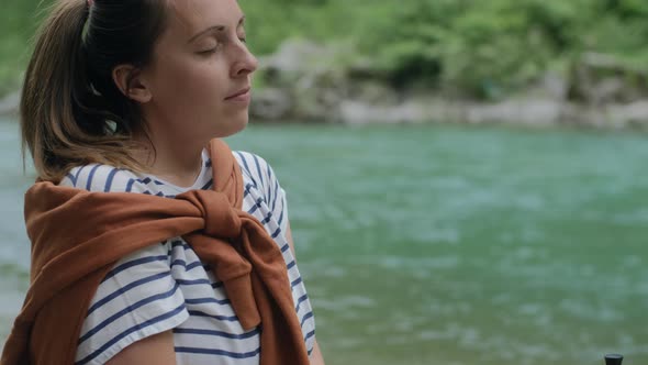 Peaceful travel woman deeply breathes and sits near mountain river.