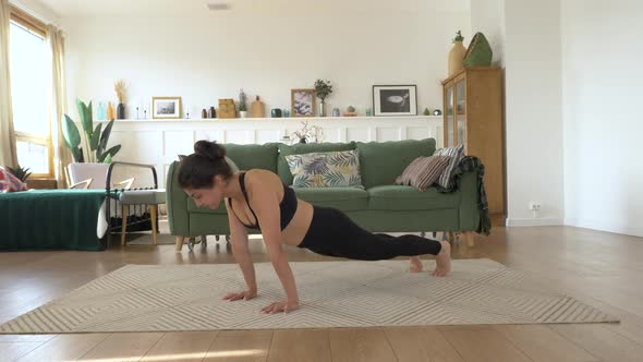 Girl is stretching on carpet in living room. Sporty woman is doing yoga poses in dynamic