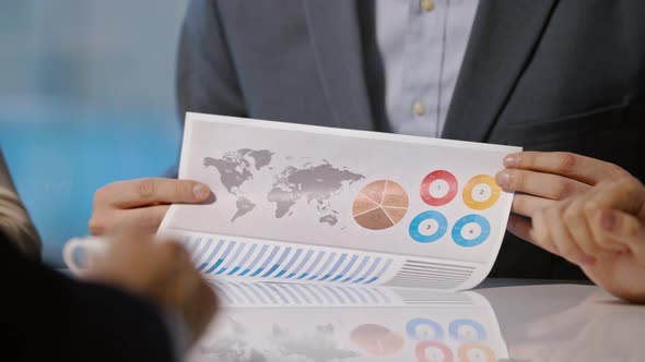 Young businessman in suit holding company development chart and telling colleagues strategy