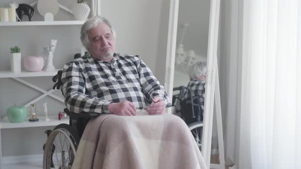 Elderly Caucasian Grey-haired Man Sitting in Wheelchair and Signing. Old Male Retiree Suffering From