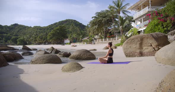 Female Seats on the Empty Beach, She Makes Yoga Practice in the Morning