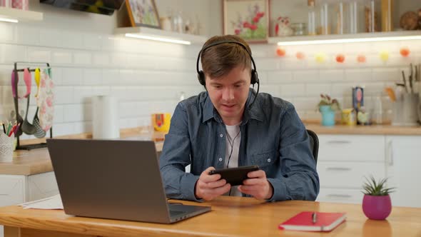 Happy man is playing video game at home using modern smartphone touching screen