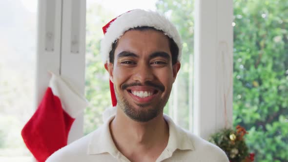 Portrait of happy biracial young man in santa hat at home during christmas