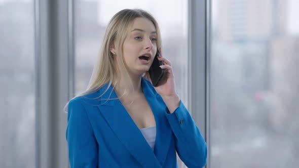 Angry Young Businesswoman Talking on the Phone Gesturing Looking Out the Window Indoors