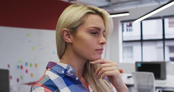 Caucasian businesswoman rubbing her chin in thought and smiling in office