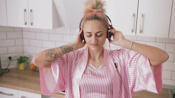 Happy Young Woman with Pink Hair Dancing in Kitchen Wearing Pink Pajamas and Listening to Music with