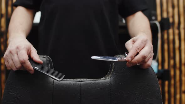 Haircut master puts his hands with scissors for milling and a hair clipper on the barber chair