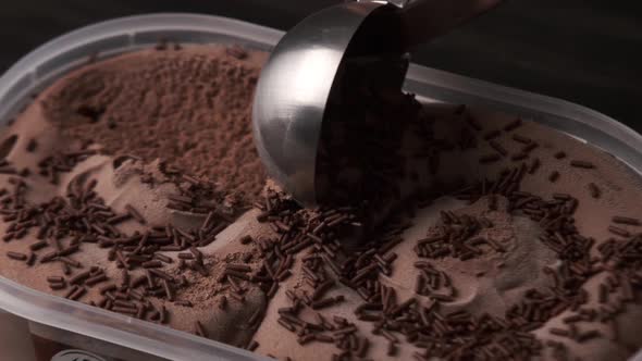 Close up view of a person scooping up chocolate ice cream from a tray.