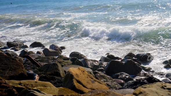 A big ocean wave crashing and in slow motion against a rocky California beach and spraying white wat