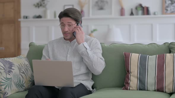 Man with Laptop Talking on Phone on Sofa