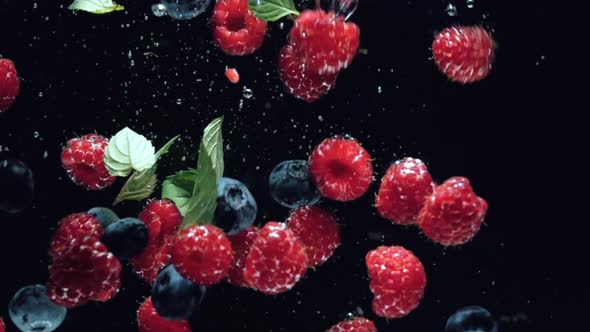 Fresh Raspberries with Blueberries and Fresh Mint Leaves Fall on a Black Background Into the Water