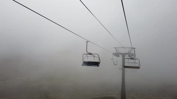 Clouds Enveloping Modern Ropeway with Benches in Amazing Mountainous Terrain