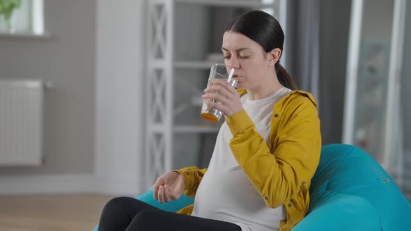 Side View Pregnant Woman Taking in Pills Sitting on Bag Chair at Home Indoors