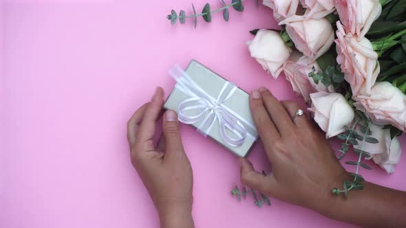 Someone Hands Wrapping Gift or Present Box and Flowers on Pink Table