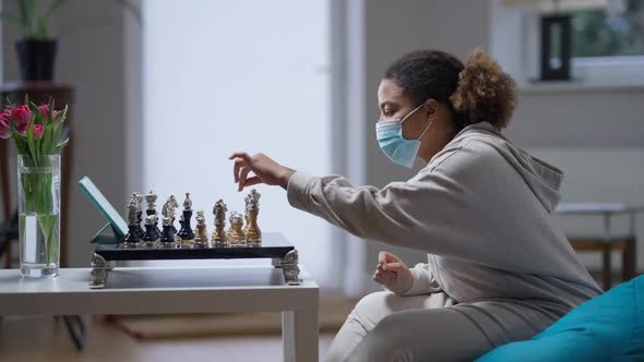 Side View of Young African American Intelligent Woman in Coronavirus Face Mask Playing Chess in