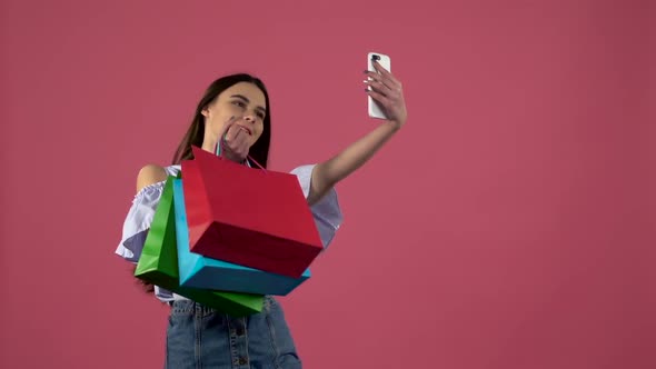 Girl Make Selfies with Colorful Packages. Pink Background. Slow Motion