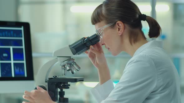 Female Scientist Using Microscope and Tablet in Laboratory