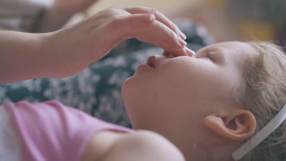 Young Mommy Massages Nose and Forehead of Girl on Bed