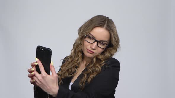 Pretty Girl Makes Selfie on Mobile Phone Then Looking Photos on Gray Background at Studio