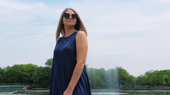 Steadicam Shot of a Beautiful Young Girl in Sunglasses in the Park Near the Fountain