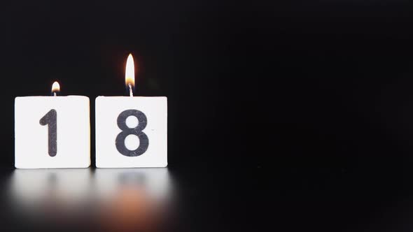 A square candle saying the number 18 being lit and blown ou