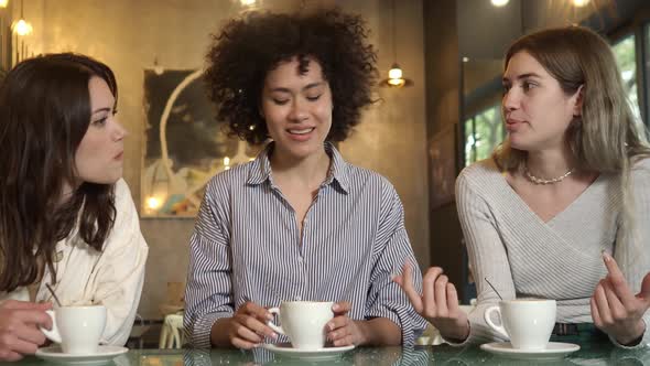 Three Smiling Multiethnic Women Friends in a Coffee Shop Drink Coffee and Toast