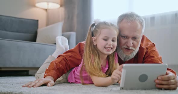 Happy Family Adult Parent Dad and Small Daughter Having Fun Using Digital Tablet Lying on Floor at