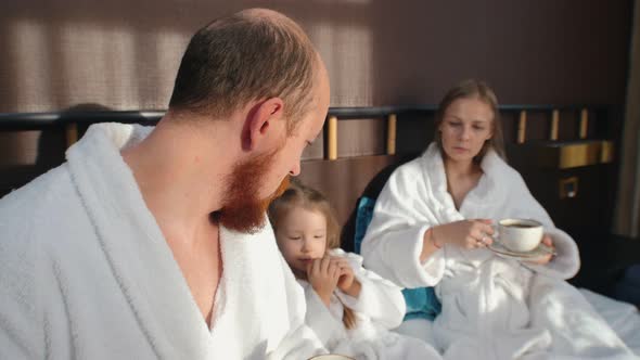 A Family in White Bathrobes Sitting in the Hotel Bed and Drinking Tea