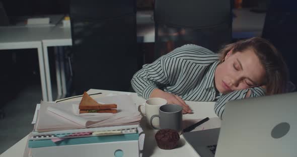 Sleepy Young Woman Office Worker Lying on Mess Table with Opened Notebook in Front of Her. Tired