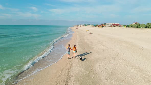 Drone Following Lovely Couple with Cute Welsh Corgi Dog Running Along Sand Beach