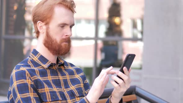 Beard Young Man Using Smartphone while Sitting Outdoor