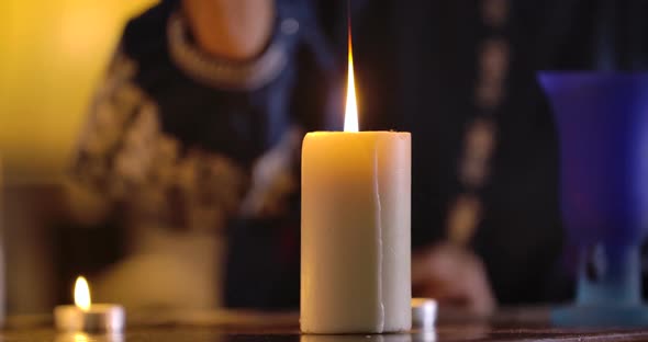 Front View of White Candle Standing on the Table and Female Caucasian Hand Lighting It Up