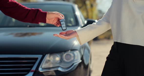 Man Hand Gives a Car Keys to Woman Hand in the Car Dealership Close Up