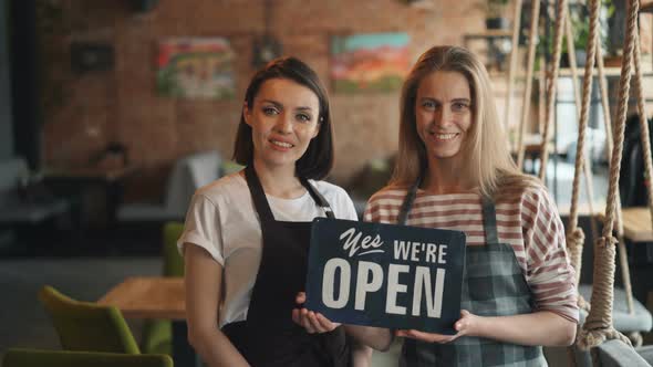 Portrait of Happy Girls Waitresses Holding We Are Open Sign Standing in Cafe