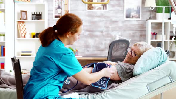 Nurse Measuring Blood Pressure of Old Sick Lady Laying in Hospital Bed