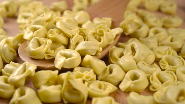 Falling dry uncooked raw tortellini pasta on a wooden spoon in slow motion