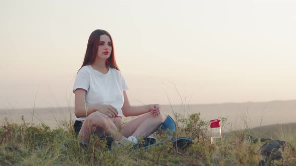 Pregnant woman is sitting on hill on yoga mat calmly and confidently looking straight, front view.