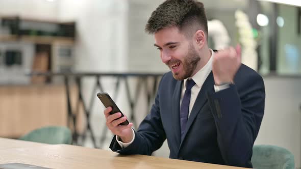 Young Businessman Celebrating Success on Smartphone in Office