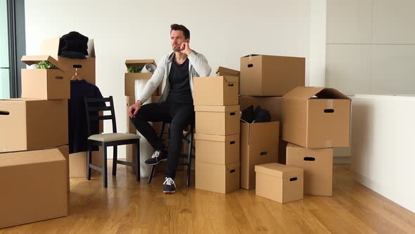 A Moving Man Sits on a Chair in an Empty Apartment and Thinks About Something, Surrounded By Boxes