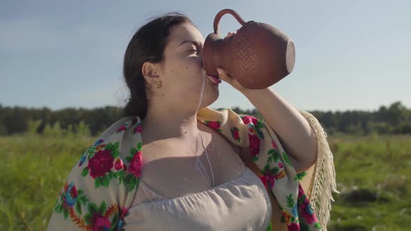 Cute Overweight Woman Enjoys Drinking Fresh Milk From the Earthen Jug on the Green Summer Field