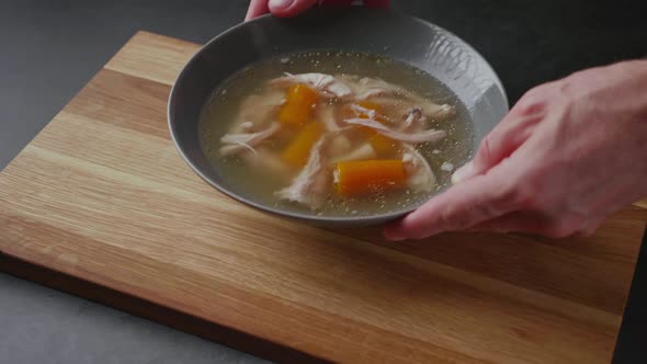 Serving fresh hot healthy paleo chicken broth soup to wooden board on concrete background.