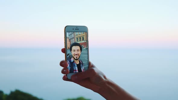 Hand Holding Smartphone During Video Call with Man in Front of the Sea