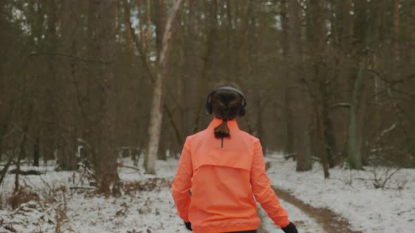 Woman running in winter park with headphones and wearing orange finished training hard breathing